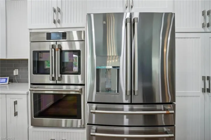 Kitchen featuring decorative backsplash, appliances with stainless steel finishes, and white cabinetry