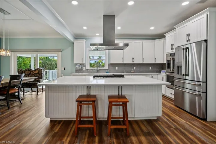 Kitchen with island exhaust hood, dark hardwood / wood-style flooring, appliances with stainless steel finishes, and a kitchen island