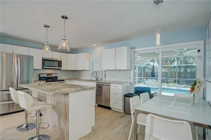 Kitchen with stainless steel appliances, decorative backsplash, a kitchen island, white cabinetry, and light stone countertops