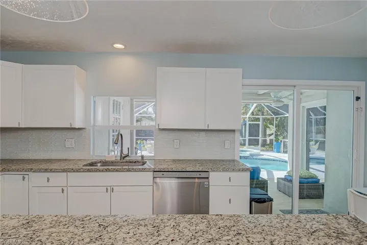 Kitchen featuring white cabinets, stainless steel dishwasher, light stone counters, healthy amount of natural light, and recessed lighting