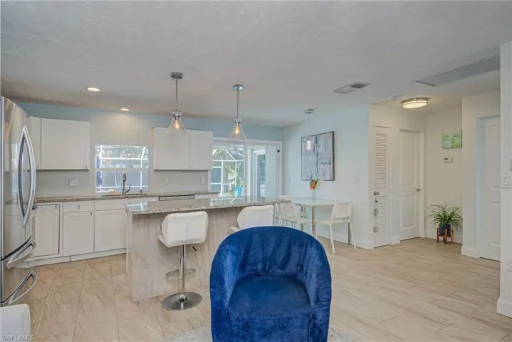 Kitchen featuring white cabinets, decorative light fixtures, light stone countertops, freestanding refrigerator, and a textured ceiling