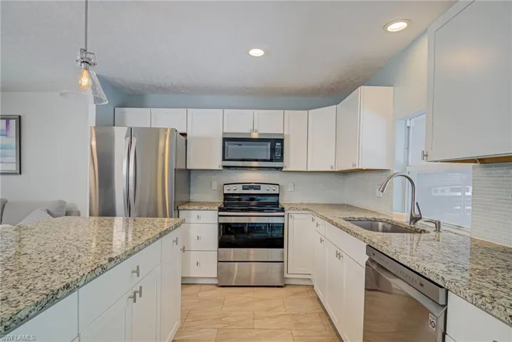 Kitchen with appliances with stainless steel finishes, white cabinets, tasteful backsplash, pendant lighting, and light stone counters
