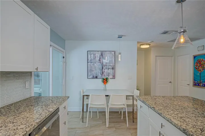 Kitchen with white cabinetry, light stone counters, pendant lighting, dishwasher, and backsplash