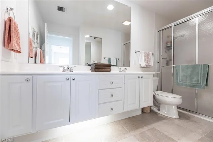 Primary Bathroom featuring tile floors, dual bowl vanity, a shower with shower door, and toilet