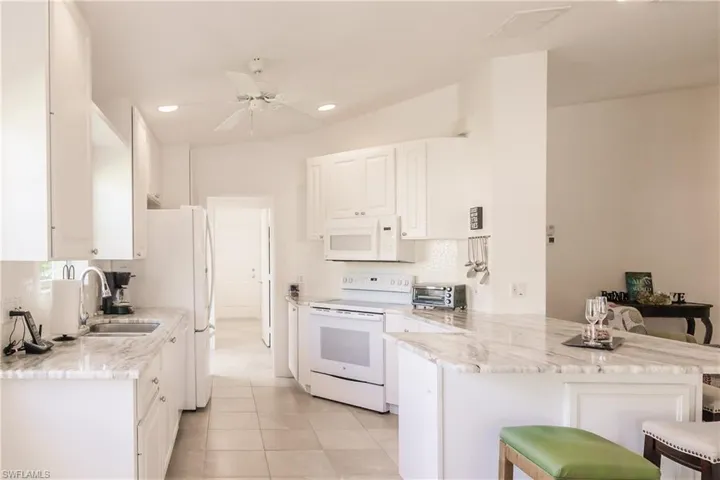 Kitchen featuring kitchen peninsula, ceiling fan, a kitchen breakfast bar, white cabinetry, and white appliances
