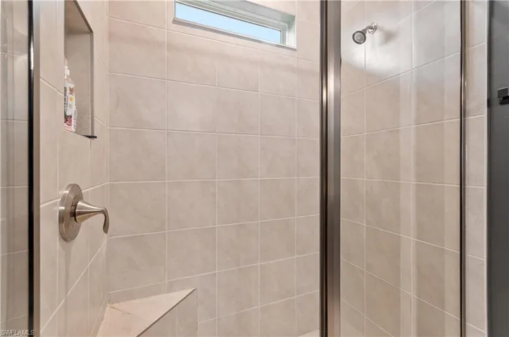 Tiled shower enclosure featuring a fixed transom window, built-in shower niche, brushed nickel fixtures, and a glass shower door