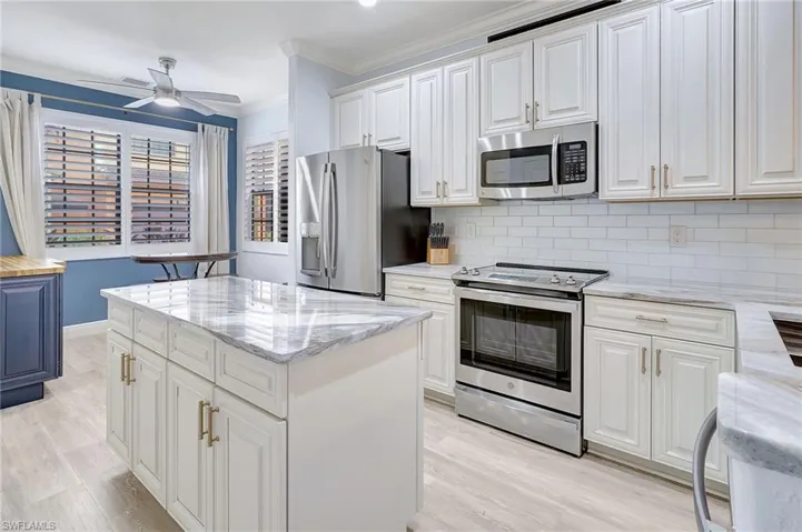 Kitchen with appliances with stainless steel finishes, light hardwood / wood-style floors, white cabinetry, a center island, and ceiling fan