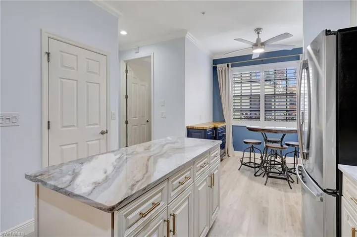 Kitchen with ceiling fan, light hardwood / wood-style flooring, a kitchen island, light stone countertops, and stainless steel fridge