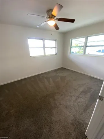 Unfurnished room featuring dark colored carpet and ceiling fan