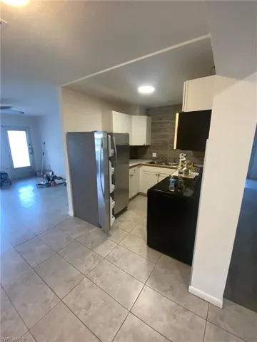 Kitchen with white cabinetry, sink, tasteful backsplash, stainless steel fridge, and light tile patterned floors
