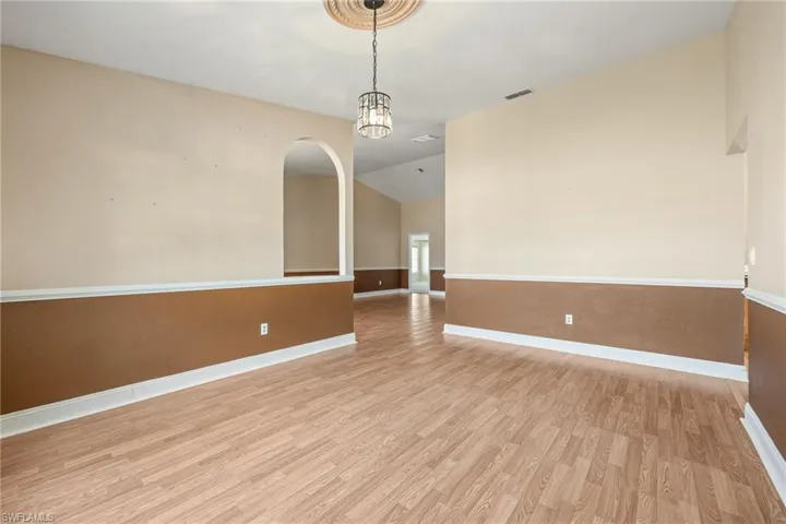 Empty room featuring light wood-style floors, baseboards, visible vents, and lofted ceiling