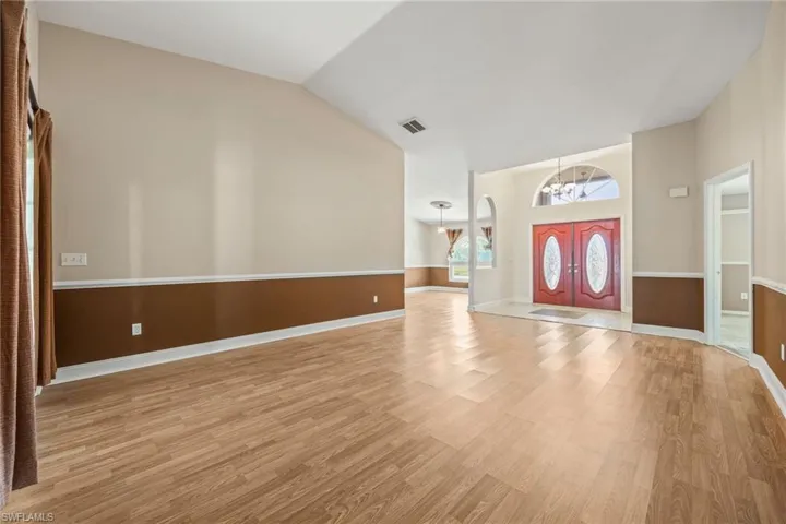 Entrance foyer with a chandelier, light wood-style flooring, baseboards, and vaulted ceiling