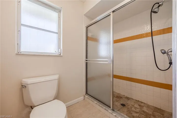 Full bathroom featuring a shower stall, tile patterned floors, baseboards, and toilet