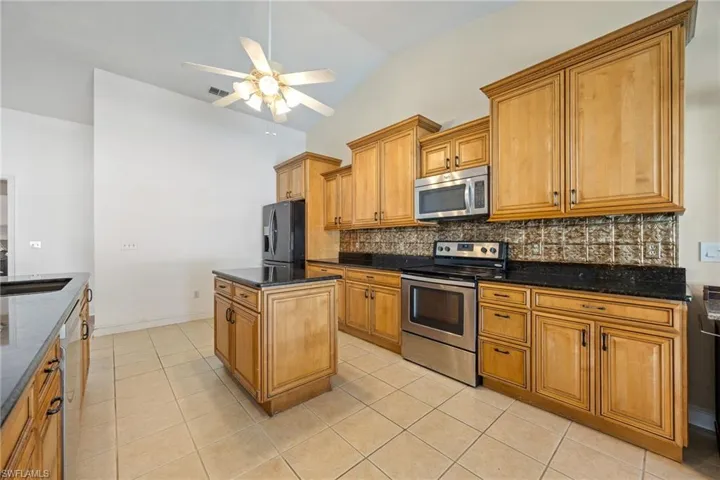 Kitchen featuring vaulted ceiling, light tile patterned flooring, decorative backsplash, appliances with stainless steel finishes, and ceiling fan