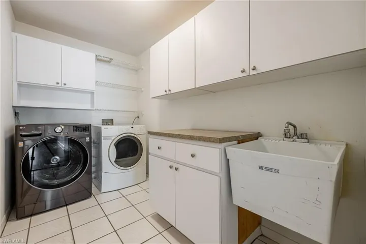 Washroom featuring washer and dryer, light tile patterned floors, a sink, and cabinet space