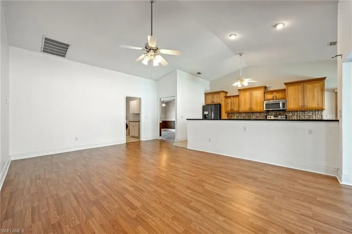 Unfurnished living room featuring visible vents, baseboards, ceiling fan, light wood-style flooring, and lofted ceiling