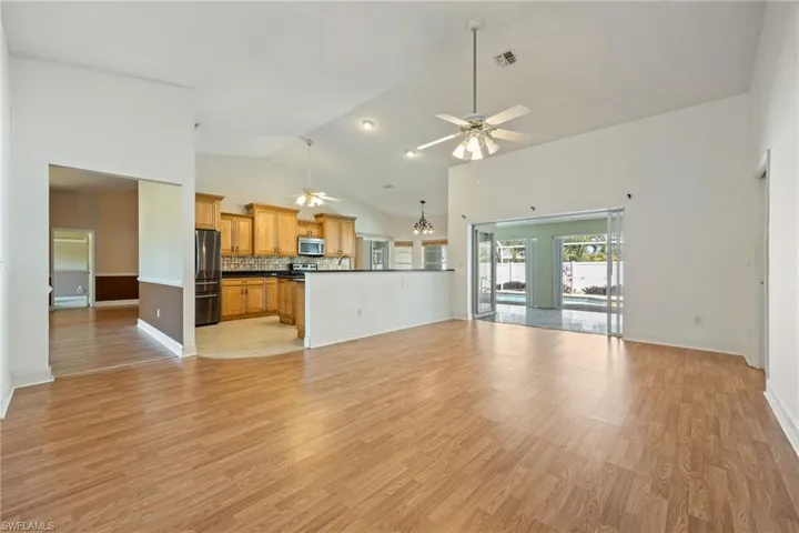 Unfurnished living room with baseboards, a ceiling fan, visible vents, high vaulted ceiling, and light wood finished floors