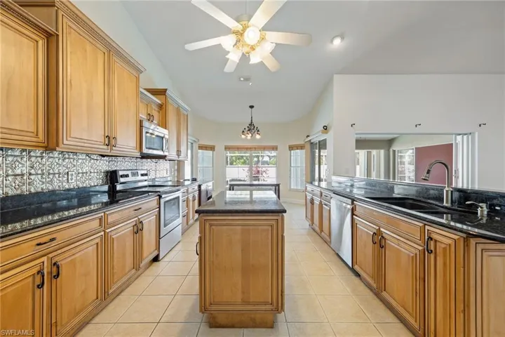 Kitchen featuring backsplash, a kitchen island, dark stone counters, stainless steel appliances, and a sink