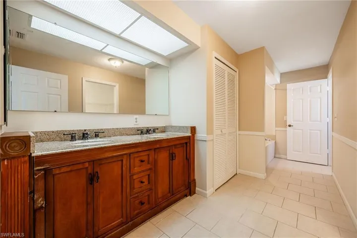 Bathroom featuring a closet, double vanity, tile patterned flooring, a bath, and a sink