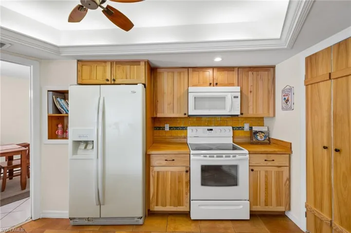 Kitchen featuring ceiling fan, white appliances, light tile floors, and tasteful backsplash