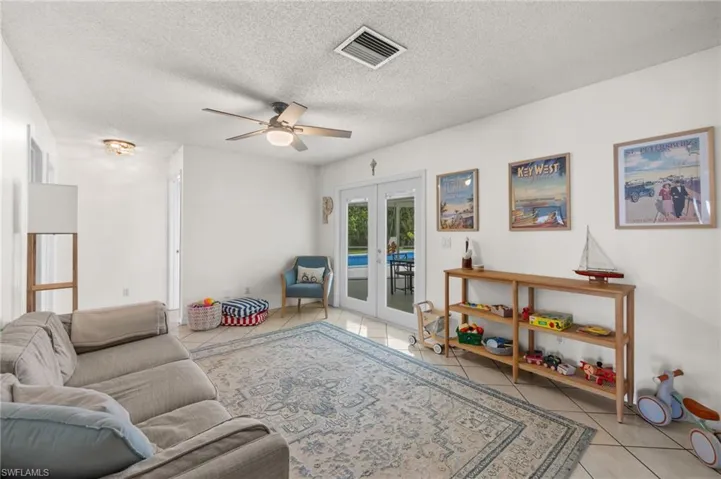 Tiled living room featuring ceiling fan, a textured ceiling, and french doors