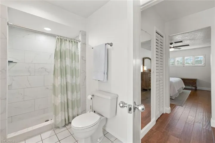 Bathroom with curtained shower, ceiling fan, toilet, and hardwood / wood-style flooring