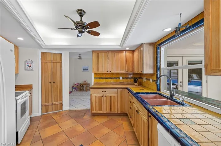 Kitchen featuring a tray ceiling, tasteful backsplash, ceiling fan, and tile countertops
