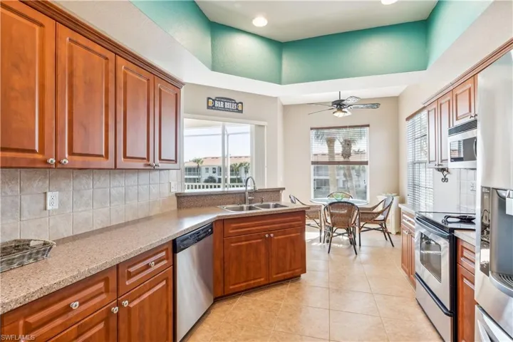 Kitchen featuring sink, ceiling fan, light tile patterned floors, appliances with stainless steel finishes, and light stone counters