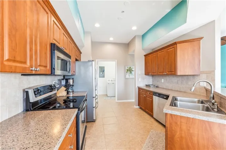 Kitchen featuring backsplash, sink, light tile patterned flooring, washer / dryer, and stainless steel appliances