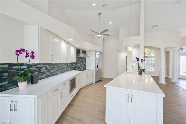 Newer Kitchen featuring tasteful backsplash, lLux vinyl flooring, wall chimney range hood, and ceiling fan
