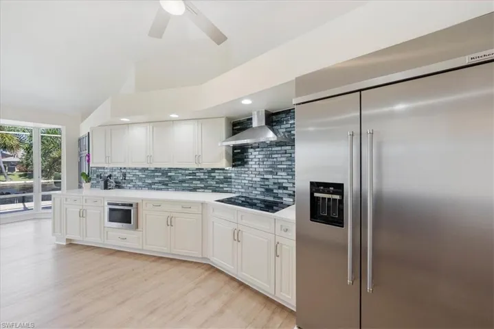 Newer Kitchen featuring built in refrigerator, tasteful backsplash, Lux vinyl floors, wall chimney range hood, and ceiling fan