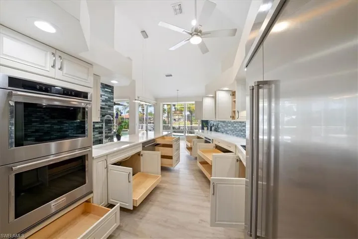 Newer Kitchen featuring tasteful backsplash, Lux vinyl flooring, wall chimney range hood, and ceiling fan, Wood pull outs everywhere!