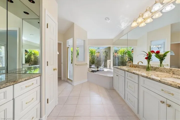 Bathroom featuring double vanity, light tile patterned floors, a stall shower, and a bath with a garden view