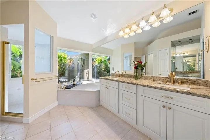Bathroom featuring double vanity, light tile patterned floors, a stall shower, and a bath with a garden view