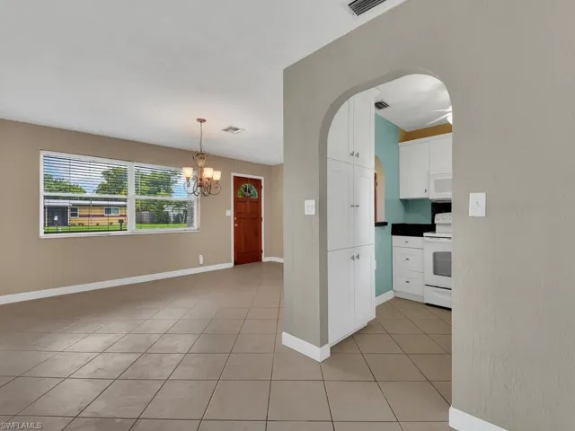 Kitchen with light tile patterned flooring, hanging light fixtures, white appliances, and white cabinets