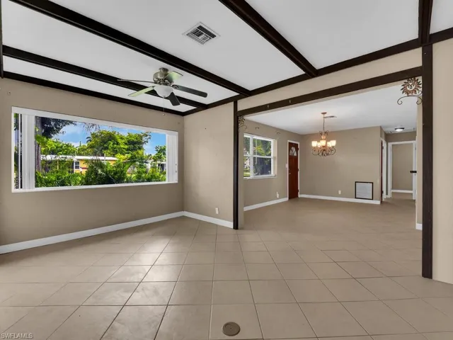Tiled empty room featuring ceiling fan with notable chandelier and beamed ceiling