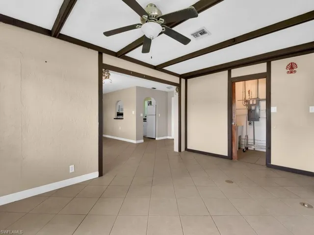Empty room with beamed ceiling, ceiling fan, and tile patterned floors