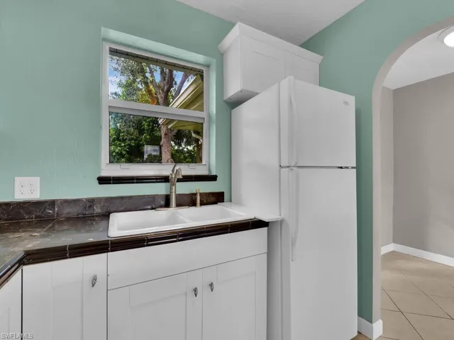 Kitchen featuring white fridge, white cabinets, sink, tile counters, and light tile patterned floors