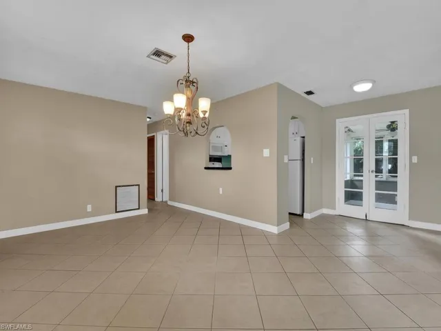 Tiled spare room with french doors and an inviting chandelier
