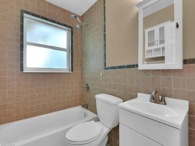 Full bathroom featuring tiled shower / bath, toilet, vanity, tile walls, and decorative backsplash