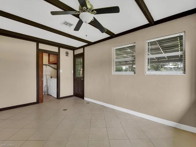Tiled spare room featuring ceiling fan, independent washer and dryer, and beam ceiling
