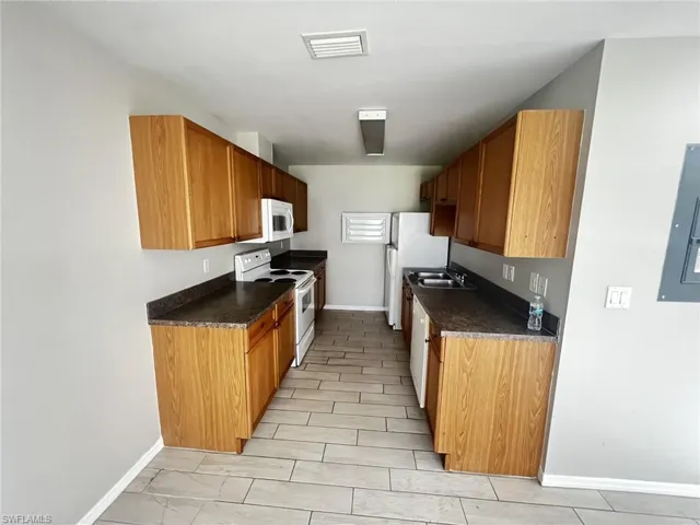 Kitchen featuring white appliances, dark countertops, electric panel, and brown cabinetry