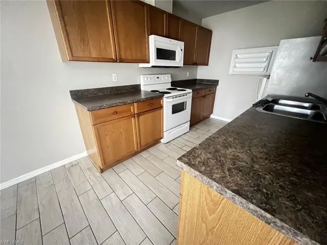 Kitchen featuring white appliances, dark countertops, and wood tiled floors