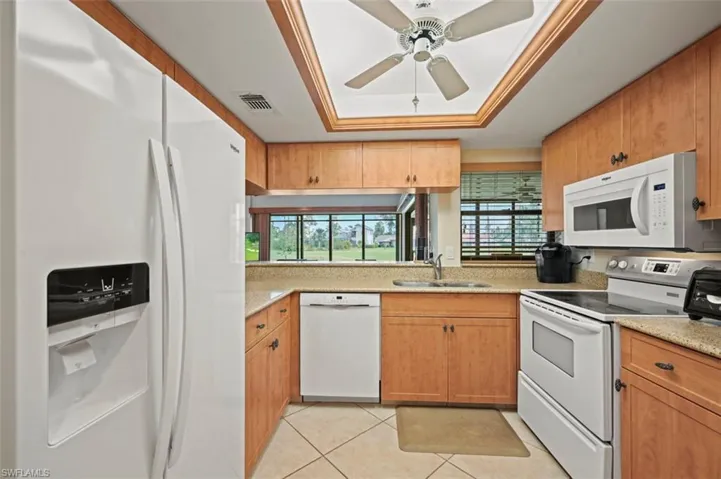 Kitchen featuring white appliances, sink, ceiling fan, light tile patterned floors, and a tray ceiling