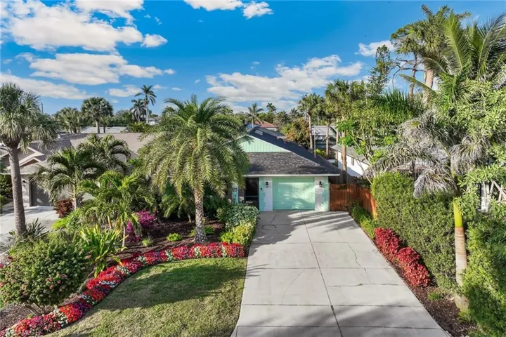 View of front of house featuring a garage, large driveway, and mature landscaping