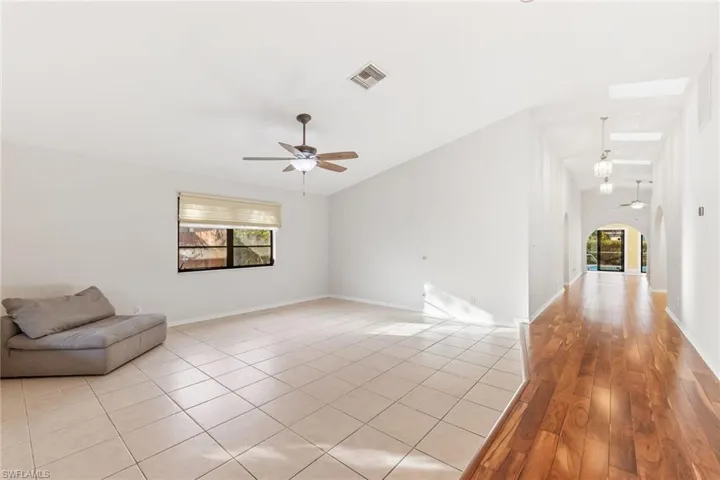 Living room featuring lofted ceiling, ceiling fan, and a mix of tile and light wood flooring
