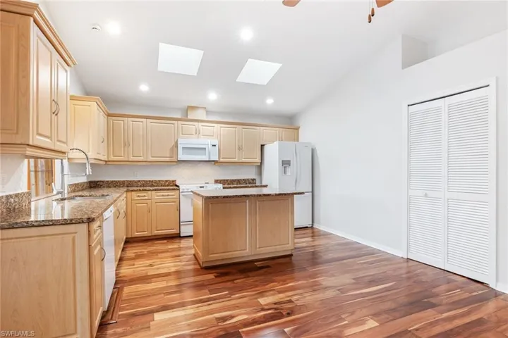 Kitchen featuring a kitchen island, light brown cabinetry, sink, stone countertops, and white appliances