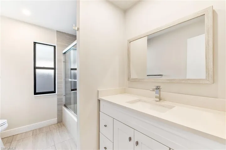 Guest bathroom featuring enclosed tub / shower combo, tiled floors, vanity, and toilet