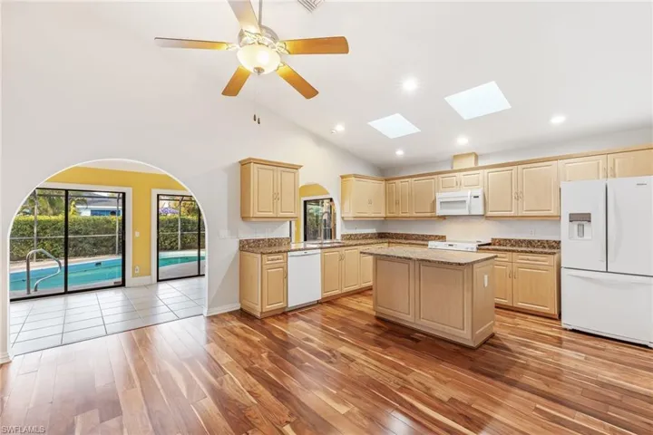 Kitchen featuring white appliances, ceiling fan, stone countertops, light brown cabinetry, a center island, and light wood flooring