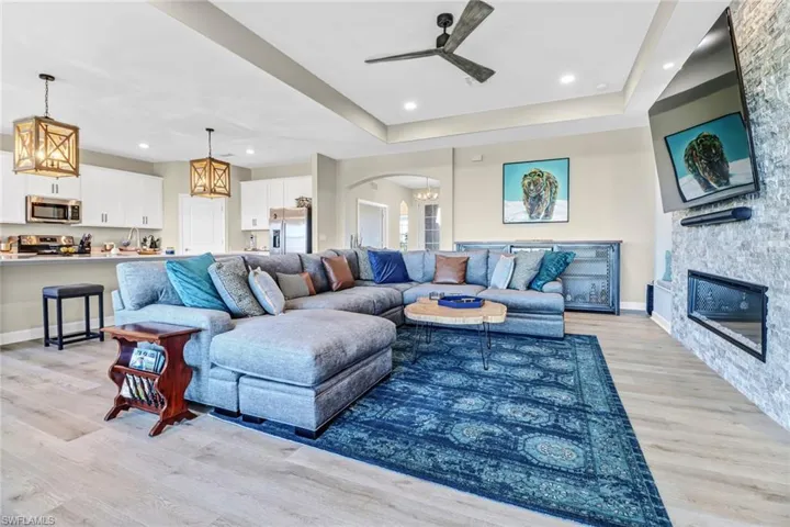Living room featuring a fireplace, light wood-type flooring, ceiling fan, and a raised ceiling